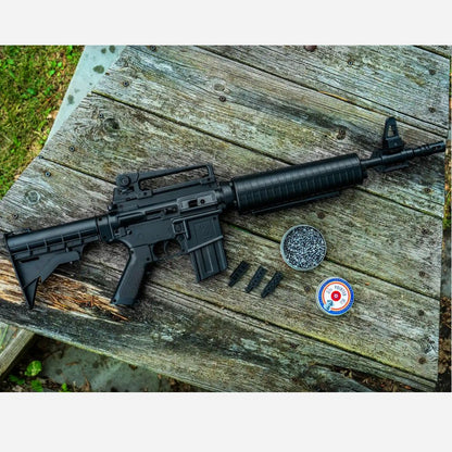 Black rifle on a wooden surface with two round objects and a circular object with a red dot.