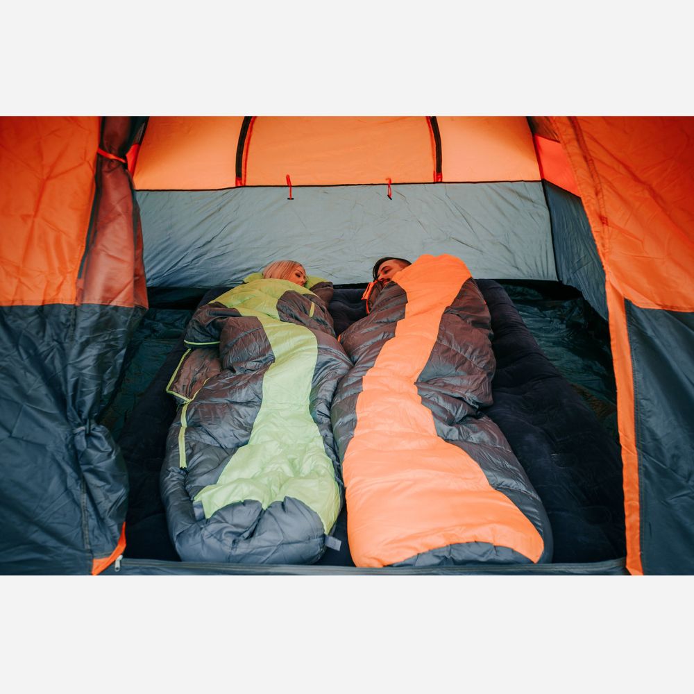 Two people sleeping in colorful sleeping bags inside an orange and gray tent.