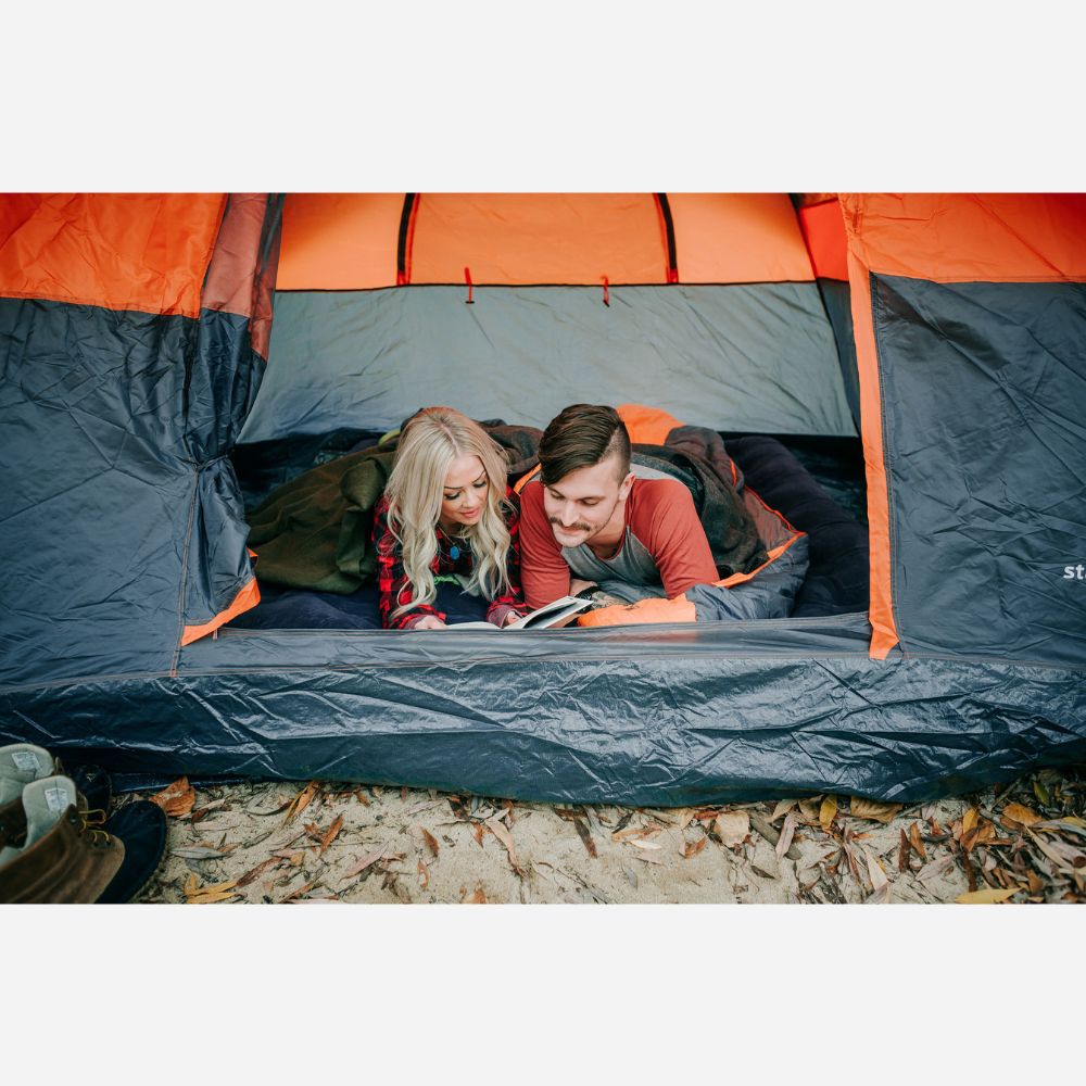 Two people inside an orange and gray tent, reading a book.