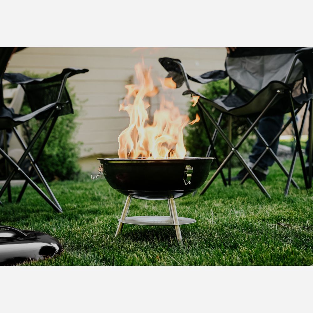 Fire pit with flames in a grassy area with folding chairs around