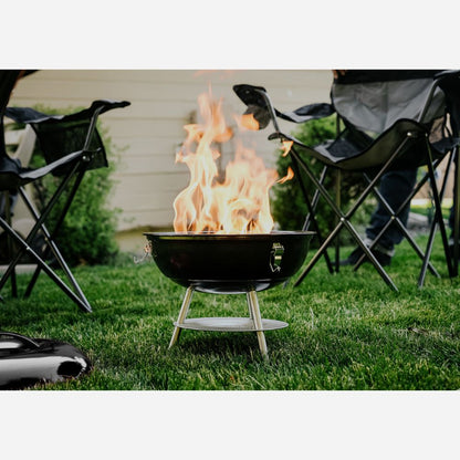 Fire pit with flames in a grassy area with folding chairs around