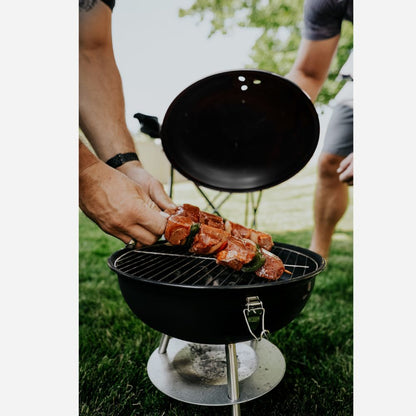 Person grilling meat on a small black portable grill outdoors.