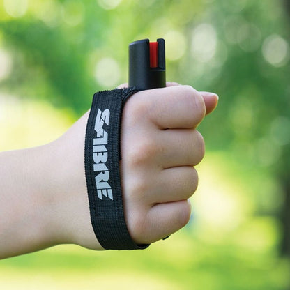 Hand holding a pepper spray device with a visible 'Sabre' brand on a blurred green background