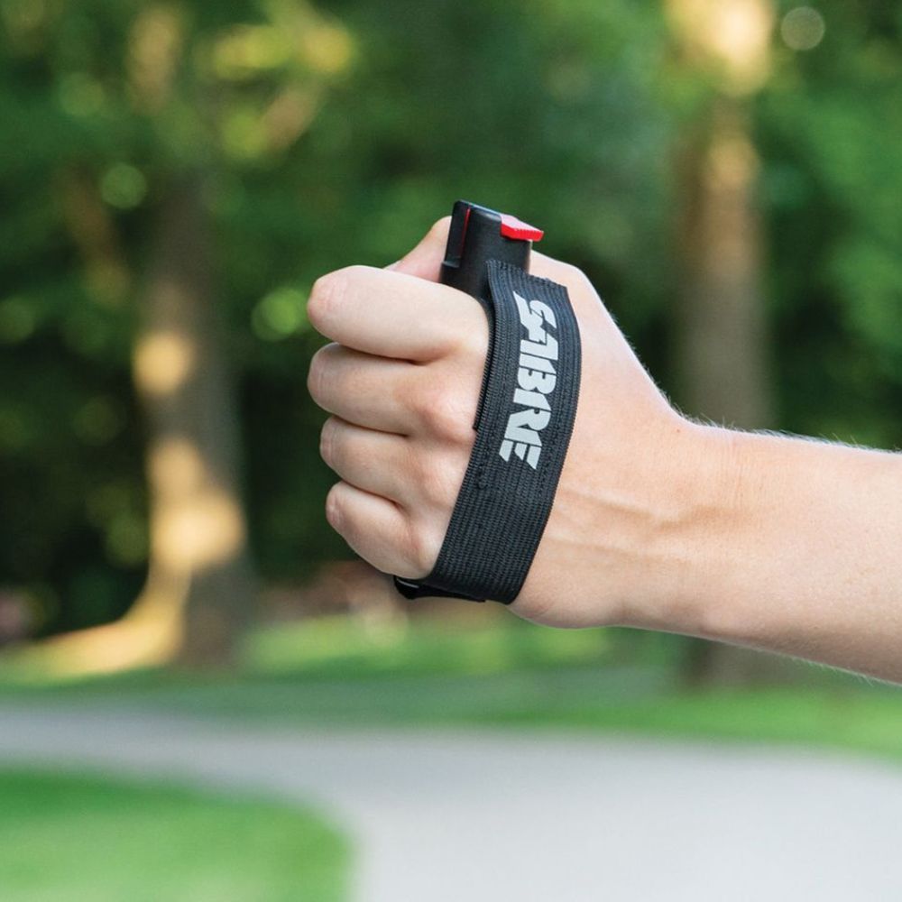 Hand holding a pepper spray device with a blurred green outdoor background