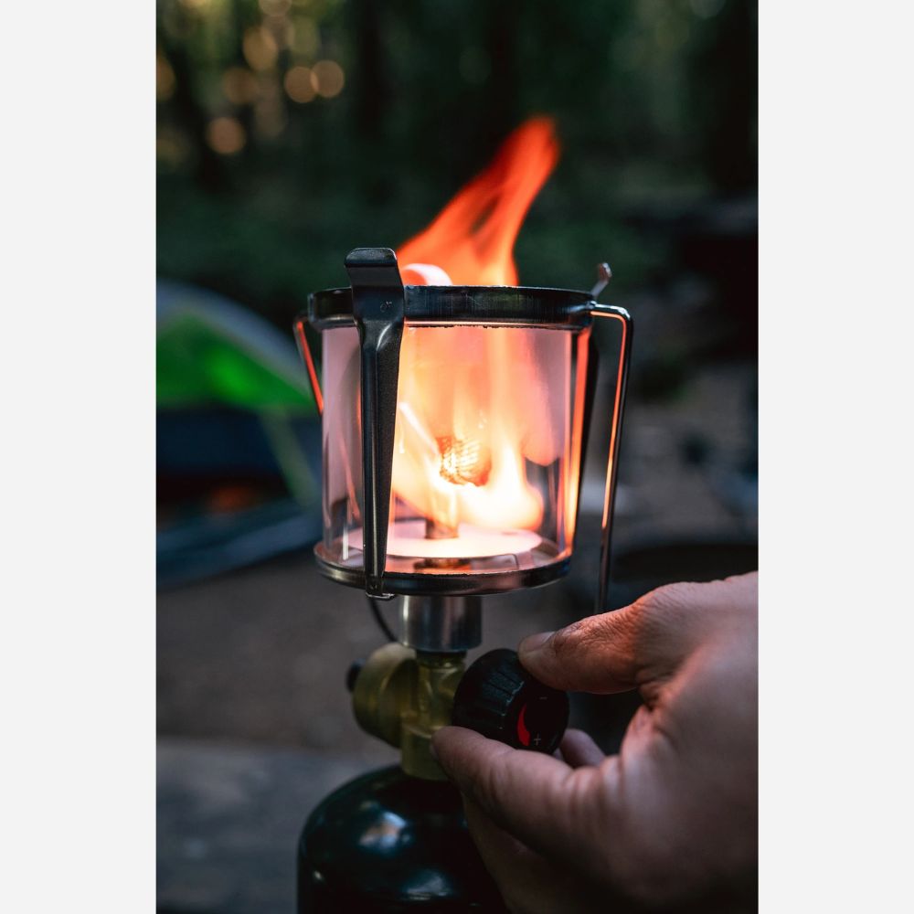 Hand holding a camping lantern with a flame against a blurred natural background