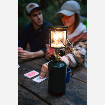 Two people sitting at a table with a lit camping lantern, playing cards.