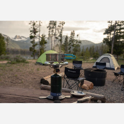 Camping scene with a portable stove and grill setup in a natural setting.