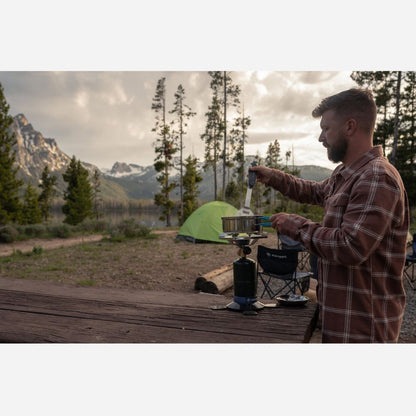 Man preparing food outdoors with a scenic mountain backdrop