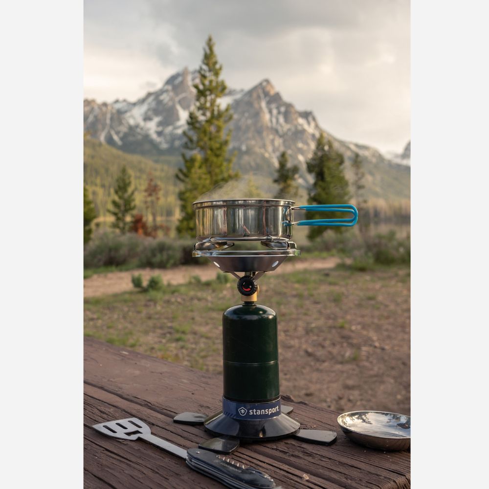 Camping stove with pot on a wooden surface against a mountainous landscape