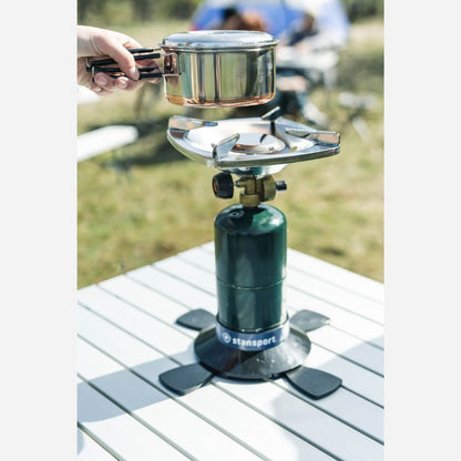 Camping stove with a pot on top, placed on a table outdoors.