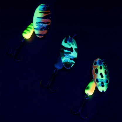 Glow-in-the-dark camo fishing spoons with treble hooks on dark background
