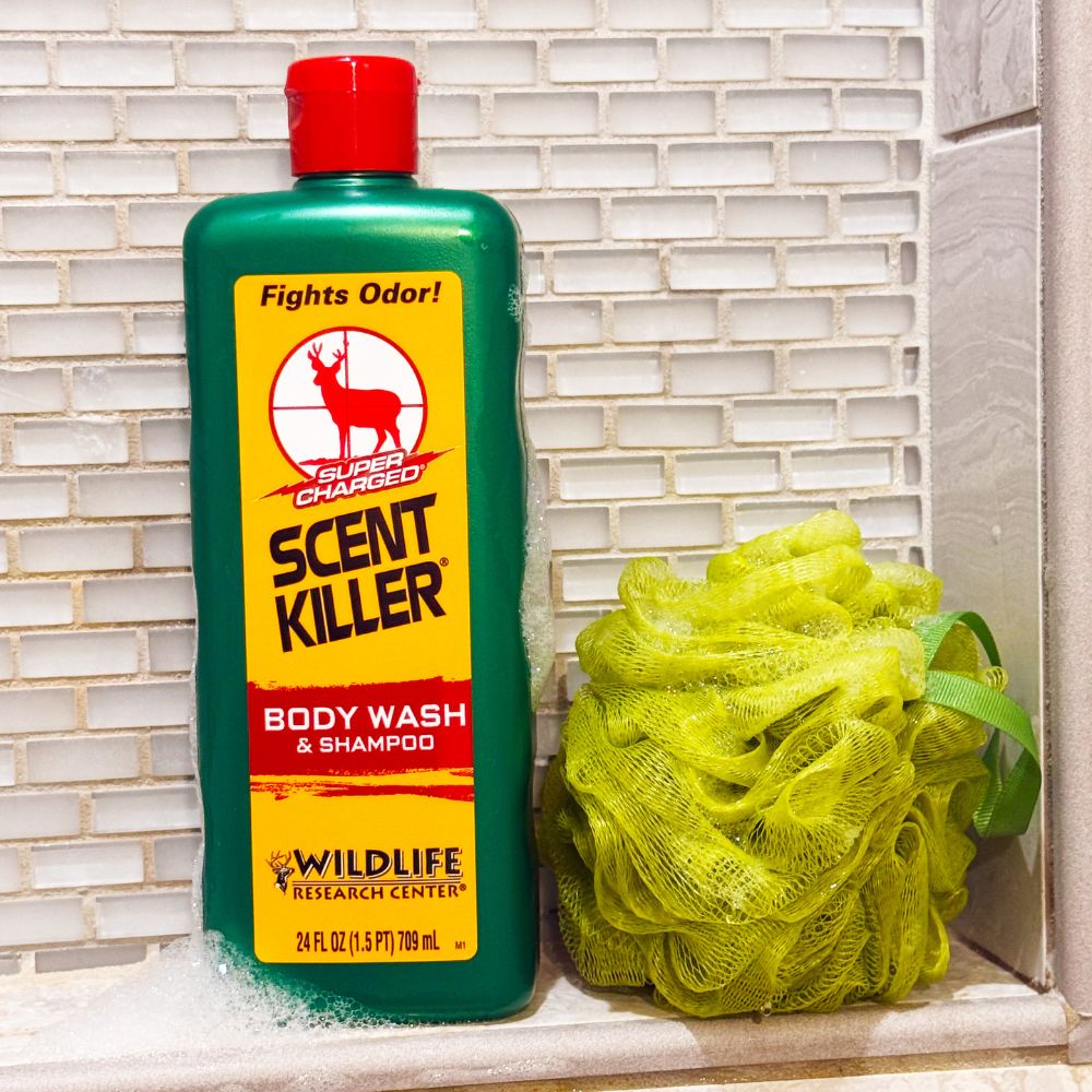 Scent Killer body wash and shampoo bottle with a yellow loofah on a tiled bathroom shelf.