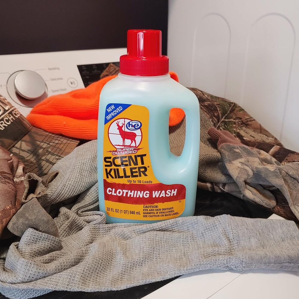 Bottle of Scent Killer Clothing Wash on a pile of clothes with a washing machine in the background.