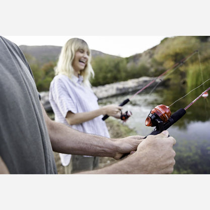 Two people fishing by a lake with mountains in the background