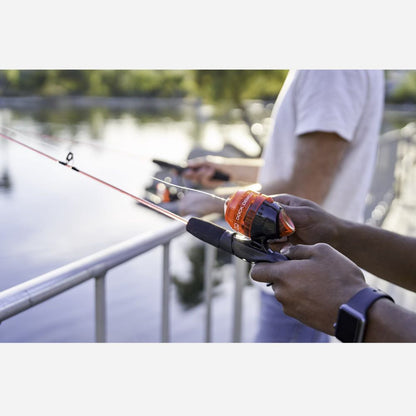 Person holding a fishing rod with an orange handle by a body of water