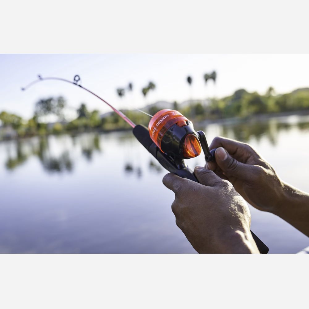 Person holding a fishing rod with an orange reel over a body of water.