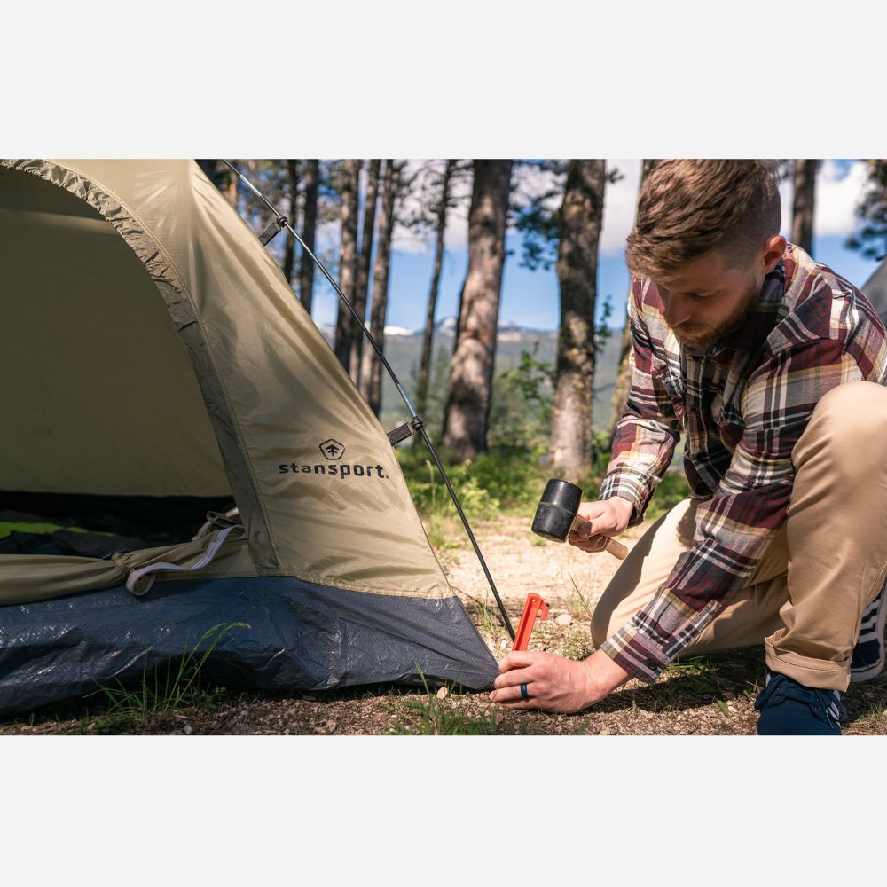 Man setting up a tent with a Stansport logo in a forested area