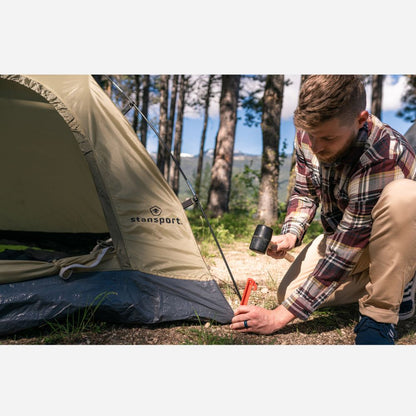 Man setting up a tent with a Stansport logo in a forested area