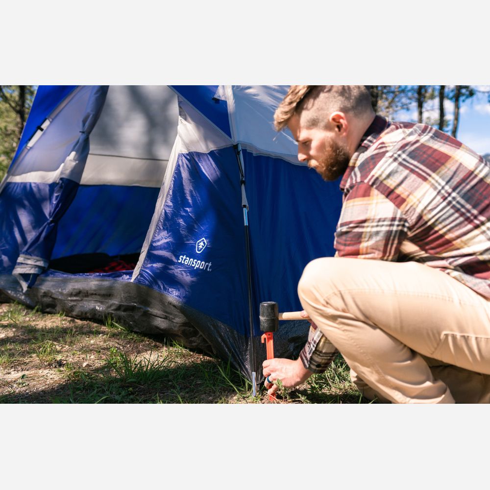 Man setting up a blue Stansport tent outdoors