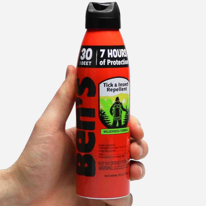 Hand holding a red and black insect repellent spray bottle with a white background