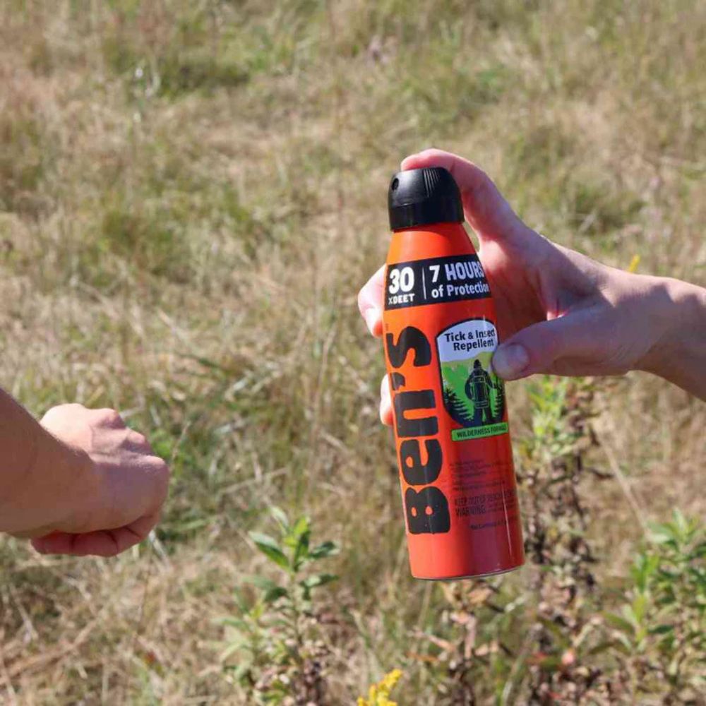 Person holding a bottle of Ben's Tick and Insect Repellent in a grassy outdoor setting