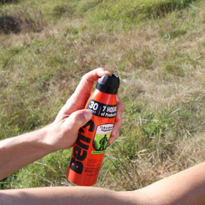 Person holding a bottle of Ben's Tick & Insect Repellent in an outdoor setting.