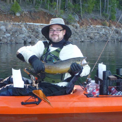 Man in kayak holding a fish on a lake with trees and rocks in the background