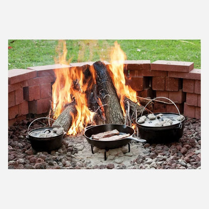 Cast iron cookware set with Dutch ovens and skillet cooking meat over an outdoor brick fire pit with burning logs.