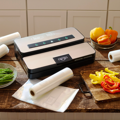 Vacuum sealer on a kitchen counter with vegetables and rolls of plastic wrap.