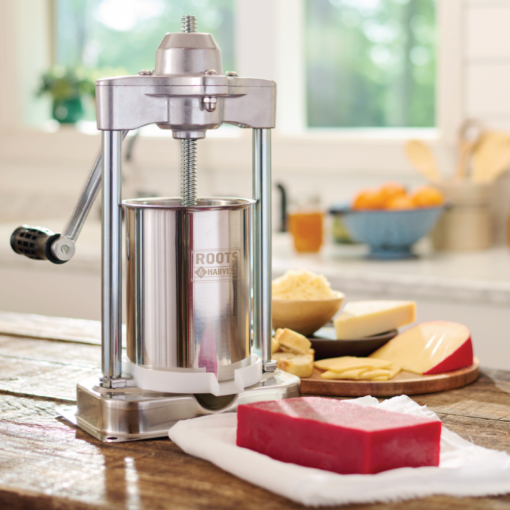 Stainless steel cheese grater on a kitchen counter with cheese and fruits in the background