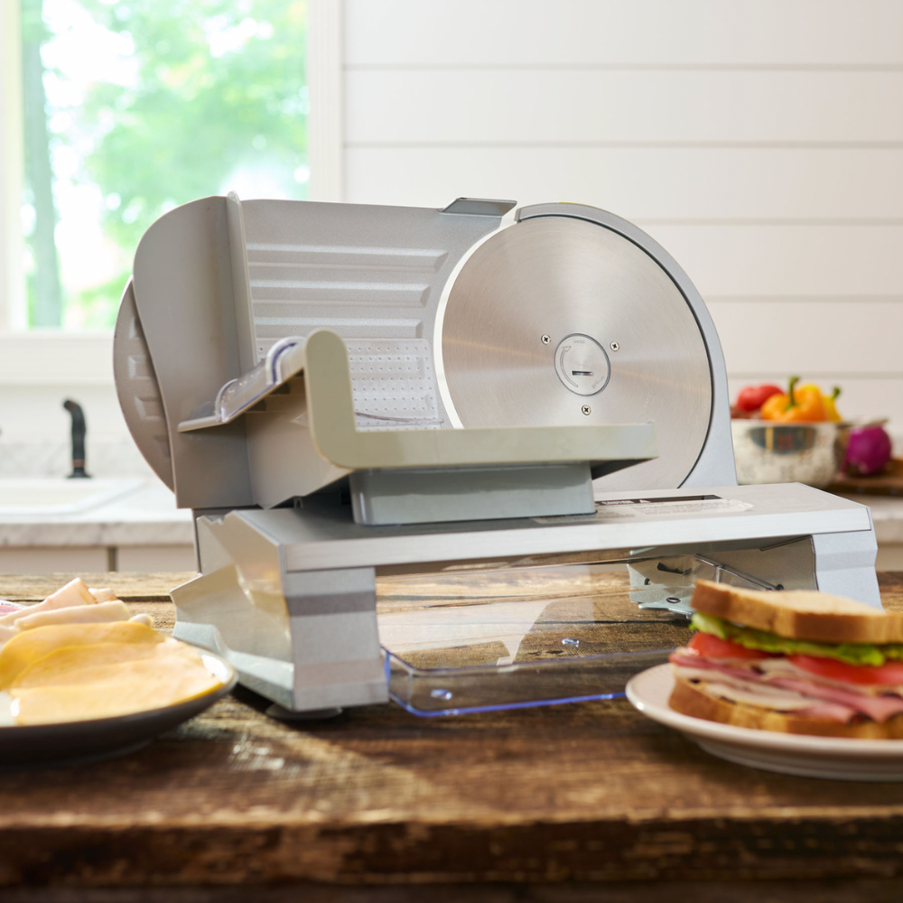 Meat slicer on a kitchen counter with a sandwich and fruits in the background