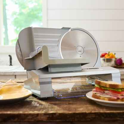 Meat slicer on a kitchen counter with a sandwich and fruits in the background