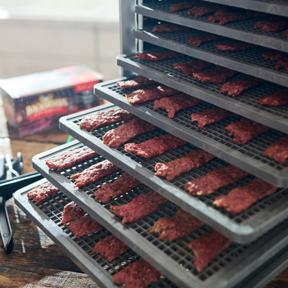 Dehydrator with trays of dehydrated meat on a wooden surface.