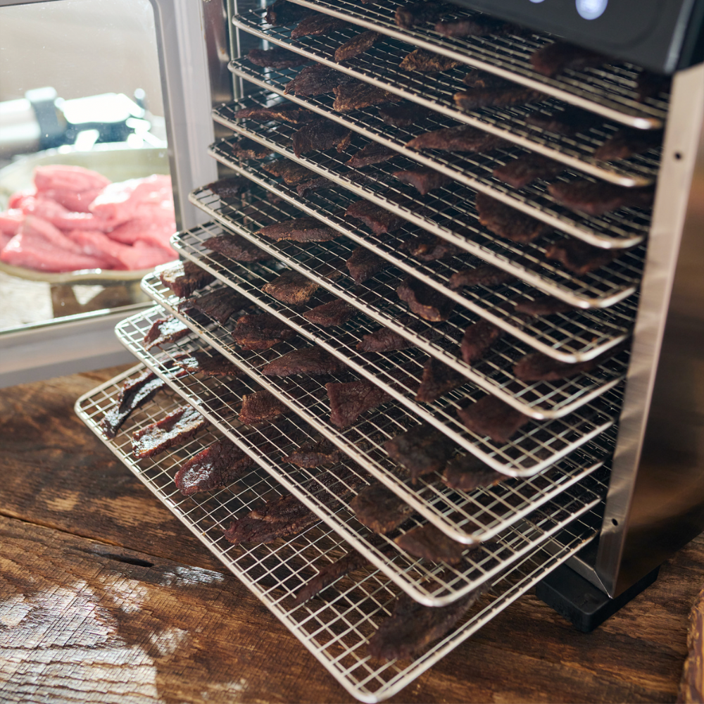 Dehydrator with racks of dehydrated meat on a wooden surface
