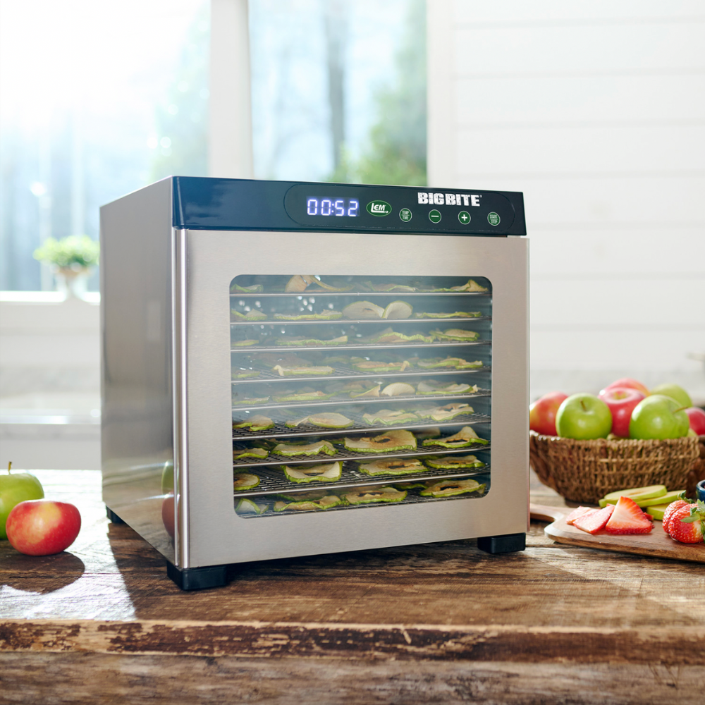 Food dehydrator with dried fruits and vegetables on a wooden table.
