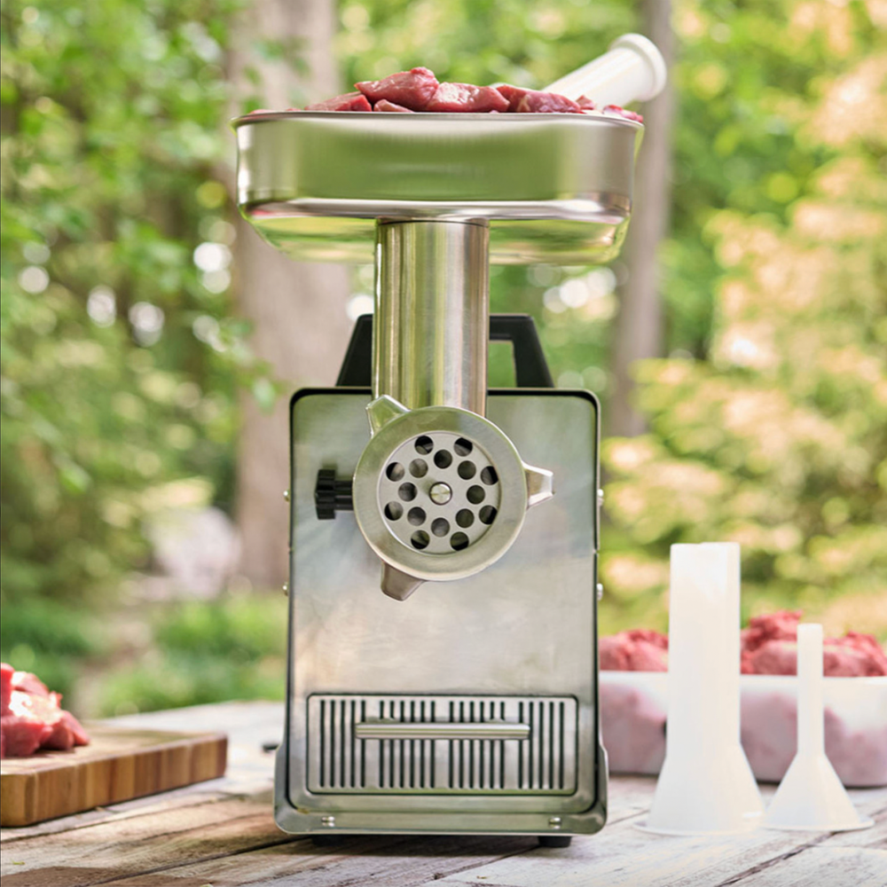 Manual meat grinder with ground meat on a wooden table outdoors