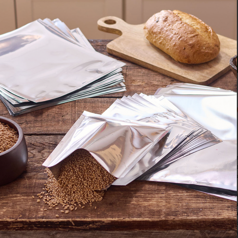Loaf of bread on a wooden cutting board with open bags of seeds on a wooden table.