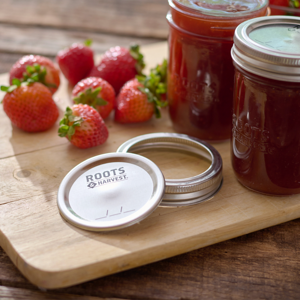Jars of jam with strawberry on a wooden board, featuring 'Roots Harvest' brand.