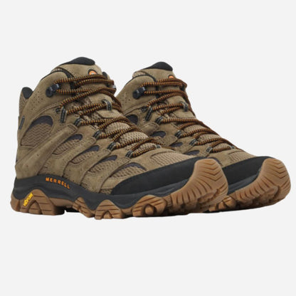 A pair of Merrell mid-height hiking boots in a brown and tan colorway, featuring a suede and mesh upper, brown laces, and a black and brown outsole, shown against a light gray background.