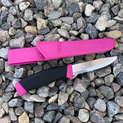 MoraKniv fixed blade knife with black and pink handle and matching pink sheath placed on gravel surface