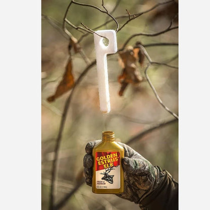 Gloved hand holding Golden Estrus Elk scent attractant bottle beneath a hanging scent wick outdoors