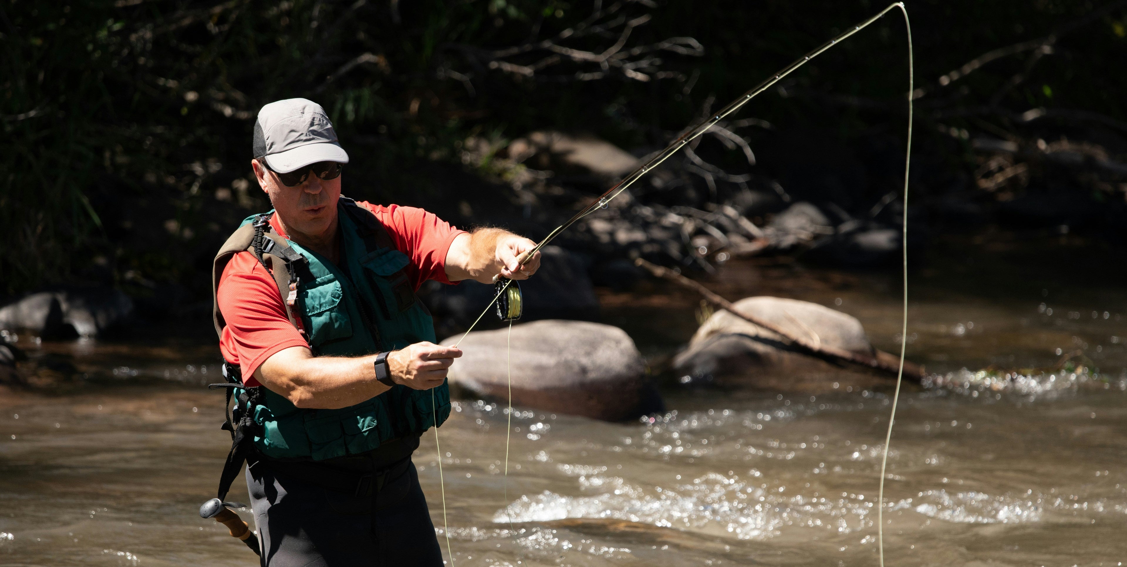 Man fly fishing in a river with trees and rocks in the background